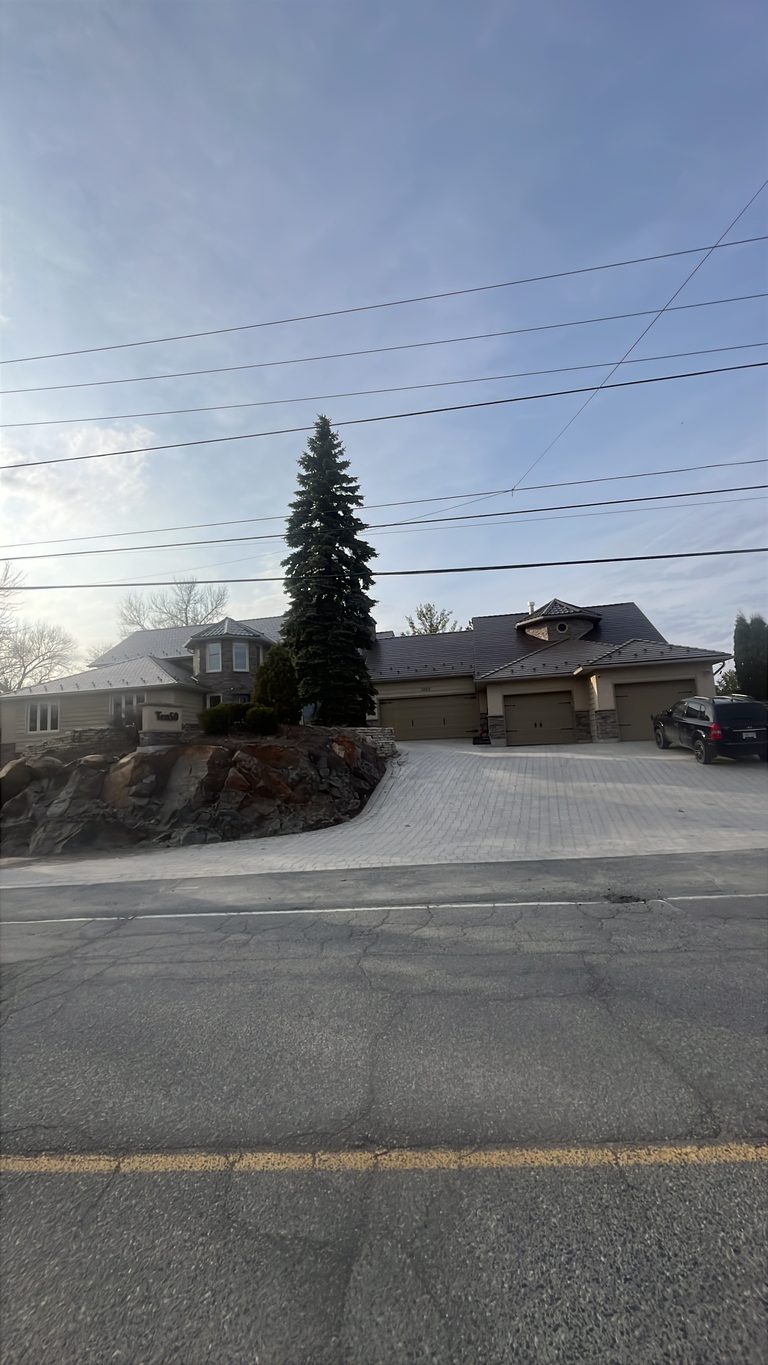 Street-view of a large suburban home in Sudbury with Interlock Colonial Brown aluminum slate roofing across a complex multi-hip profile with turret feature.