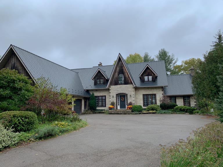 Front elevation of a Tudor-style stone home in St. George, ON featuring a steeply pitched Interlock aluminum slate roof in charcoal black with multiple dormers and complex valleys.