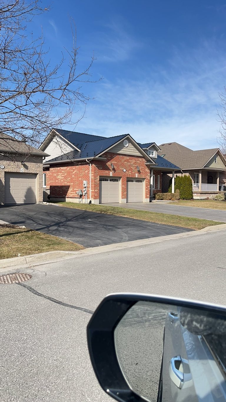 Street-view of a brick semi-detached home in Cobourg, ON featuring a black Interlock aluminum slate metal roof with multi-hip profile.