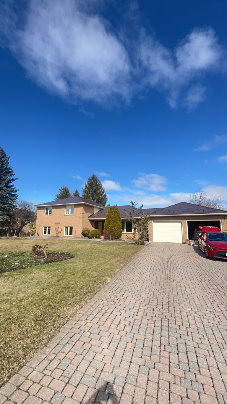 Two-storey brick Colonial home in Bradford ON with Interlock Colonial Brown cedar shingle metal roof, wide interlocking paver driveway, and attached two-car garage.