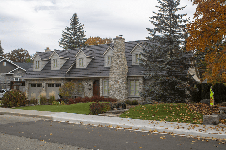 Tudor-style stone home in Waterloo ON with Interlock aluminum shake roofing in Tudor Brown, featuring multiple dormers and a prominent stone chimney.