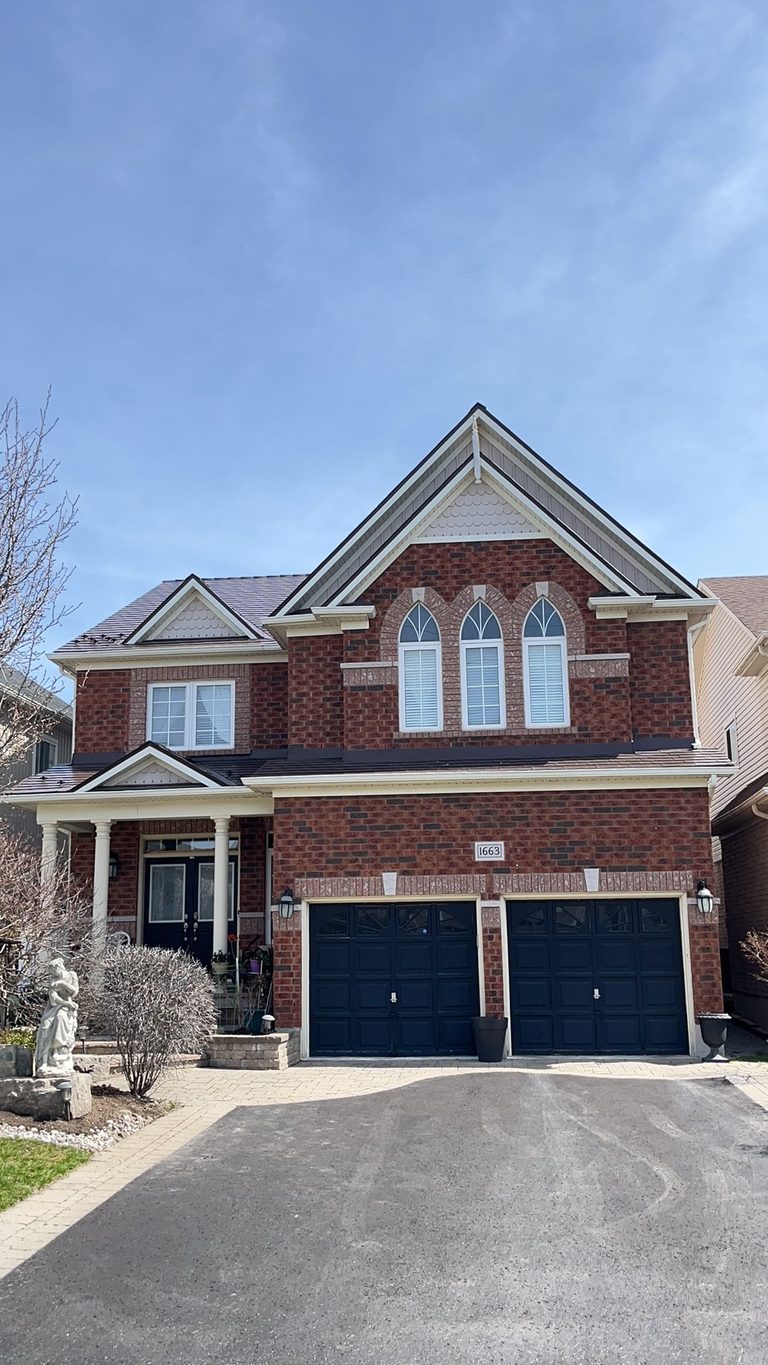 Two-storey brick Colonial home in Oshawa with Interlock aluminum slate roof in Colonial Brown, featuring multi-gable roofline and double navy garage doors.