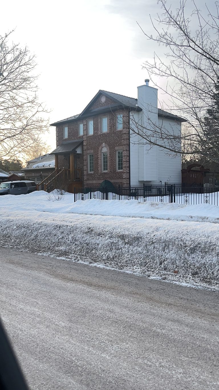Two-storey brick Colonial home in Angus ON with Interlock Colonial Brown slate metal roof, tall chimney, and iron fence, photographed from street in winter.