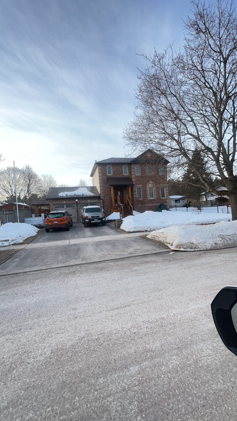 Two-storey brick Colonial home in Angus ON with Interlock Colonial Brown slate metal roofing, viewed from across a snow-covered street in winter.