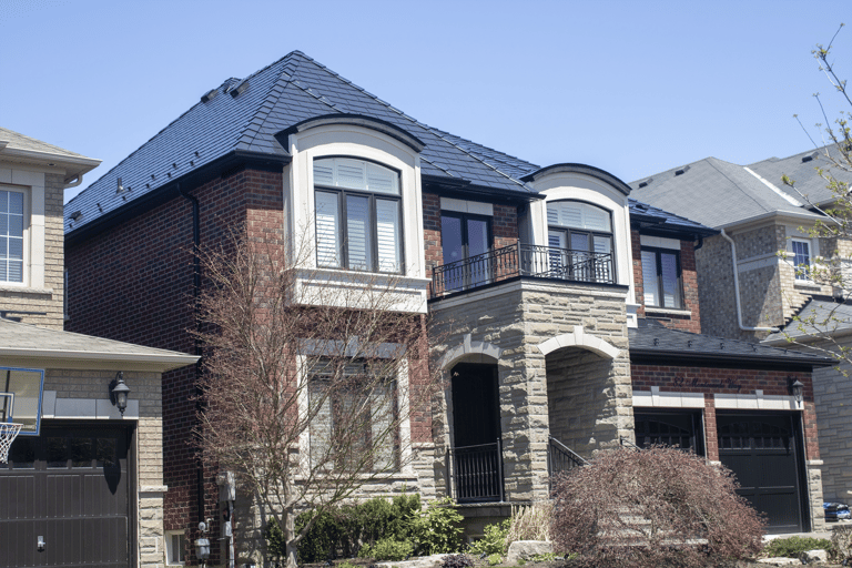 Two-storey brick and stone Colonial home in Woodbridge, ON with a complex multi-hip black Interlock aluminum slate metal roof and wrought-iron balcony.