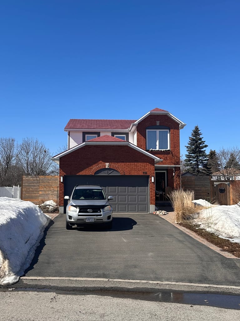Two-storey red-brick suburban home in Orleans ON with Interlock Tile Red aluminum shingle roof, multi-hip profile, and attached single-car garage.