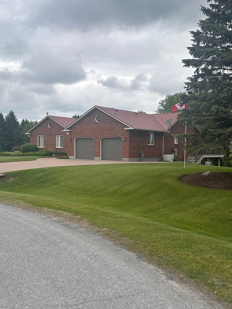 Single-storey brick ranch home in North Gower ON with Interlock Tile Red aluminum shingle roof, two-car garage, and manicured lawn.
