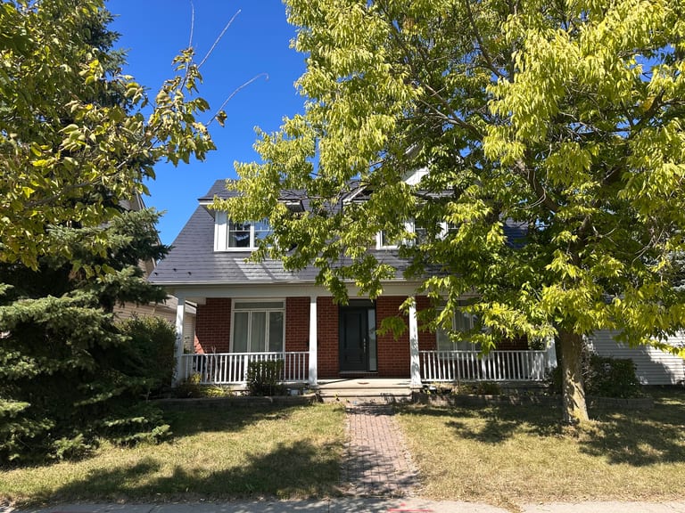 Two-storey Victorian home in Ottawa with black Interlock aluminum slate metal roofing featuring a turret and dormers, red brick facade, and covered front porch.