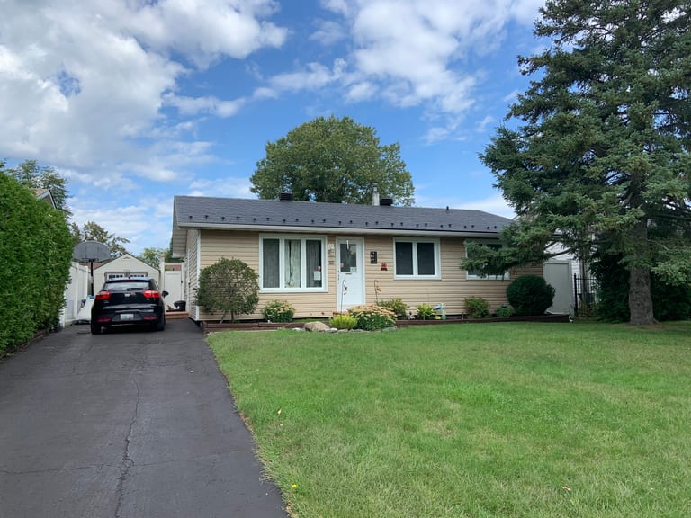 Front elevation of a single-storey ranch home in Ottawa with a black Interlock aluminum slate metal roof, beige siding, and mature trees.