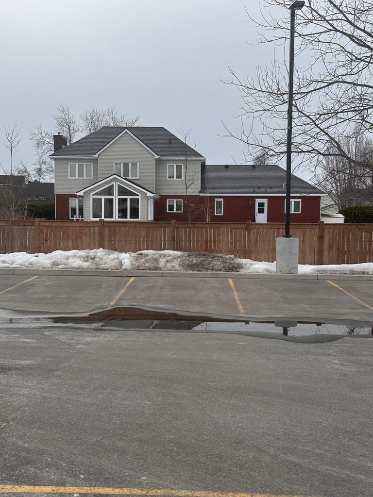 Rear elevation of a two-storey suburban home in Navan, ON with dark slate-profile Interlock aluminum roofing, red brick lower level, and gabled sunroom addition.
