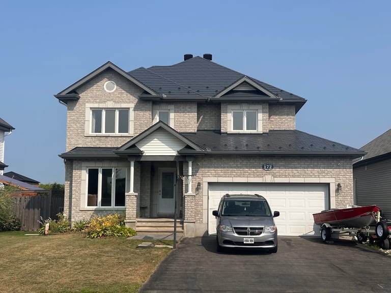 Two-storey stone suburban home with Interlock deep charcoal aluminum slate metal roof, double garage, and multi-hip roofline in Russell, ON.