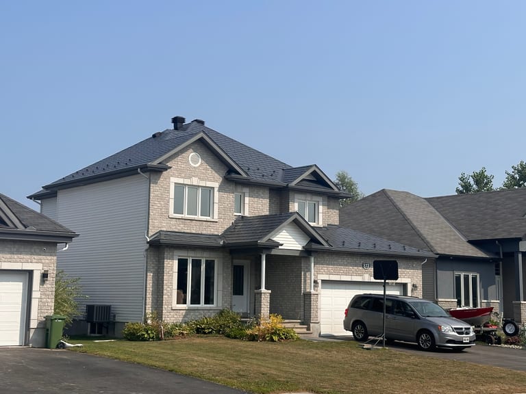 Two-storey suburban home in Russell, ON with Interlock deep charcoal aluminum slate metal roofing on a complex multi-hip roof with dormers and stone facade.