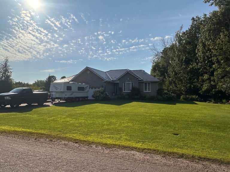 Single-storey ranch home in Pembroke ON with Interlock deep charcoal cedar shingle metal roof on a hip profile, surrounded by mature trees and lush lawn.