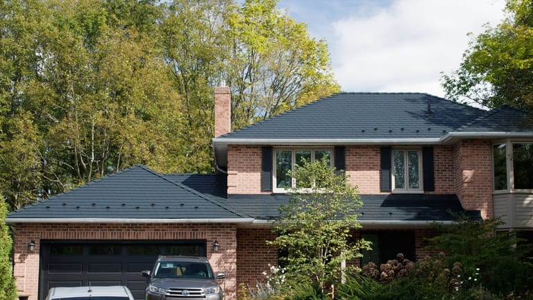 Two-storey brick Colonial home in Kingston, ON featuring a complex black Interlock aluminum slate metal roof with snow guards and brick chimney.