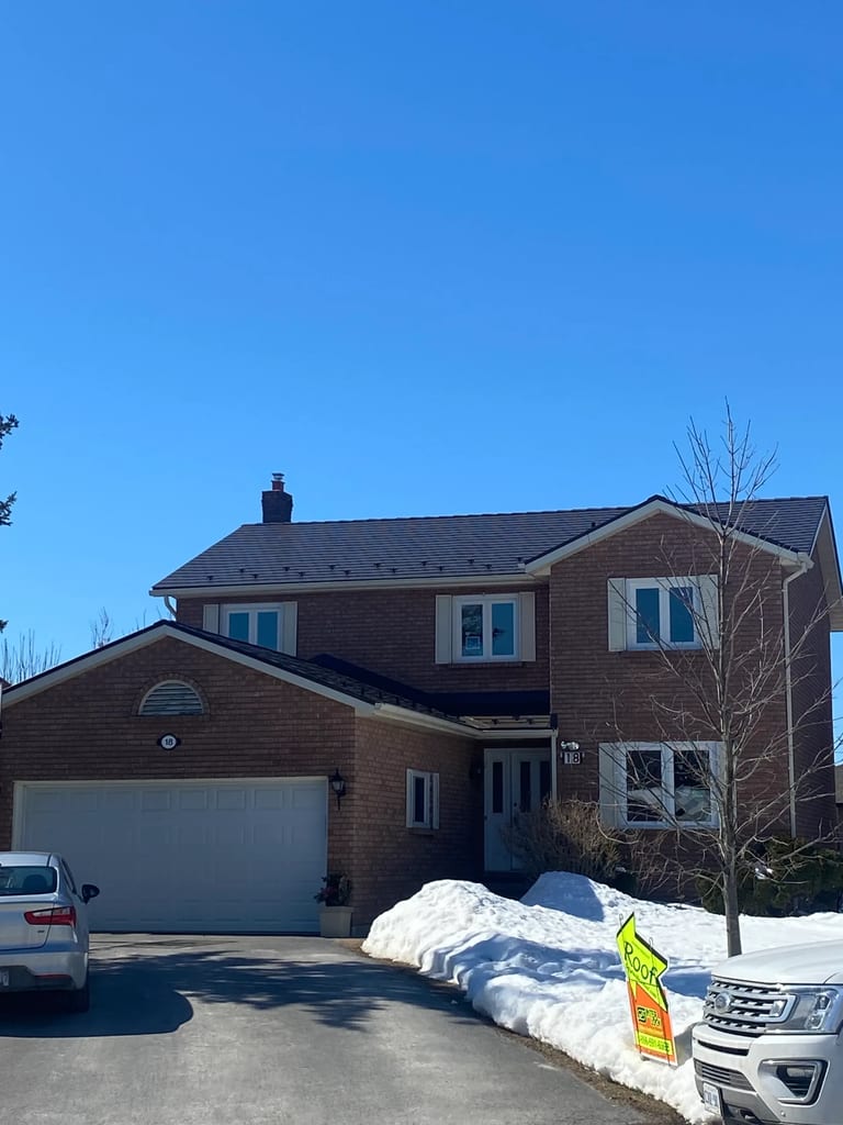Two-storey brick Colonial home in Belleville ON with Interlock Tudor Brown aluminum slate metal roof, chimney, and snow guards on a clear winter day.