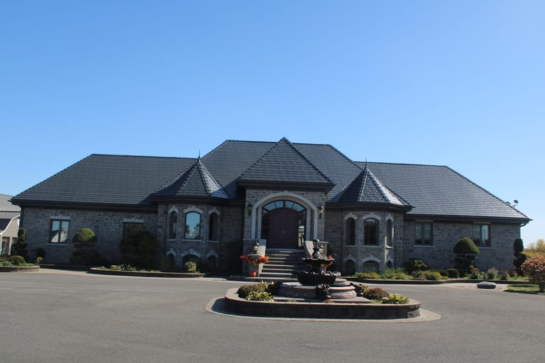 Grand single-storey stone estate in Alexandria ON featuring Interlock deep charcoal aluminum slate roofing with turreted hip roof and circular fountain driveway.