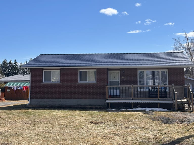 Front elevation of a brick ranch home in Chesterville, ON featuring a black Interlock aluminum slate metal roof with a low-pitch simple gable and front deck.