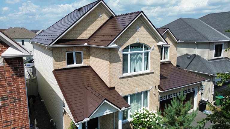 Aerial front view of a 2-storey suburban home with Interlock Colonial Brown aluminum slate metal roofing, complex multi-gable roof, and light brick exterior.