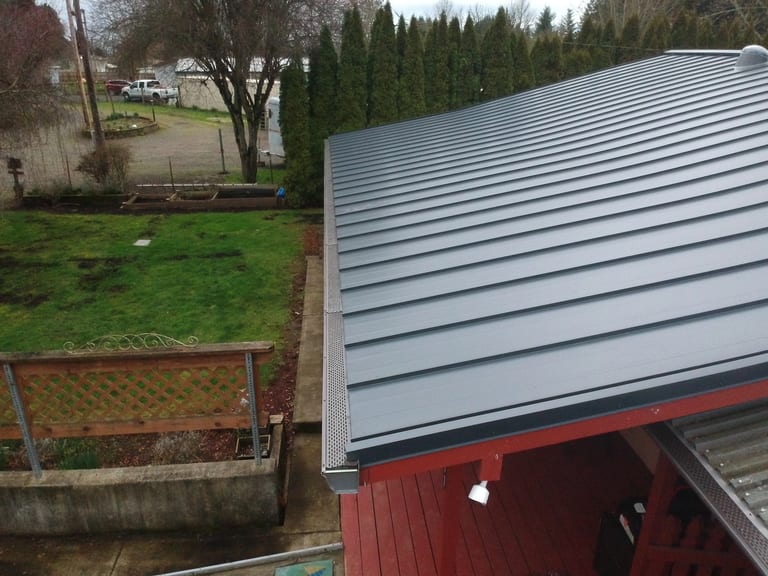 Deep Charcoal Interlock Standing Seam aluminum roof on a red single-family home among tall trees in a rural, Scio, Oregon
