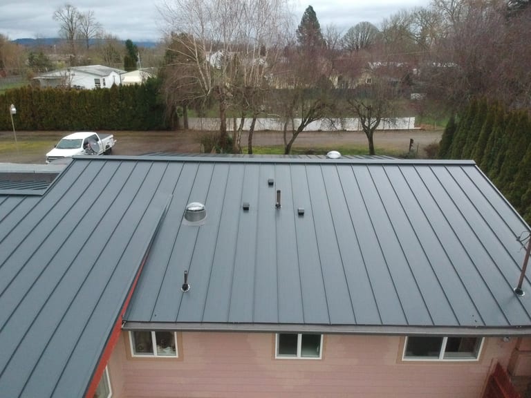 Deep Charcoal Interlock Standing Seam aluminum roof on a single-story home with a metal roof in a rural wooded area, Scio, Oregon