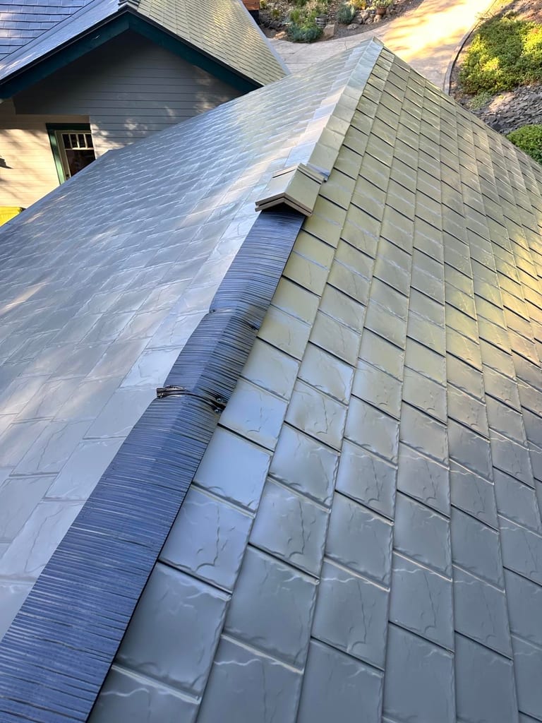 Close-up of Interlock Musket Grey aluminum slate roofing valley junction showing overlapping panels and metal flashing on a complex roof.