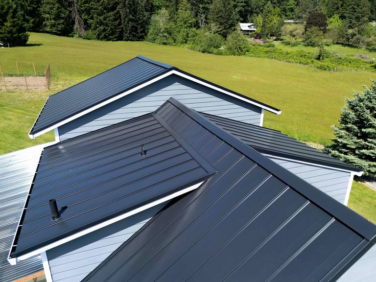 Aerial view of a black standing seam aluminum metal roof with multiple gable intersections and valley details on a rural farmhouse in Warren, OR.