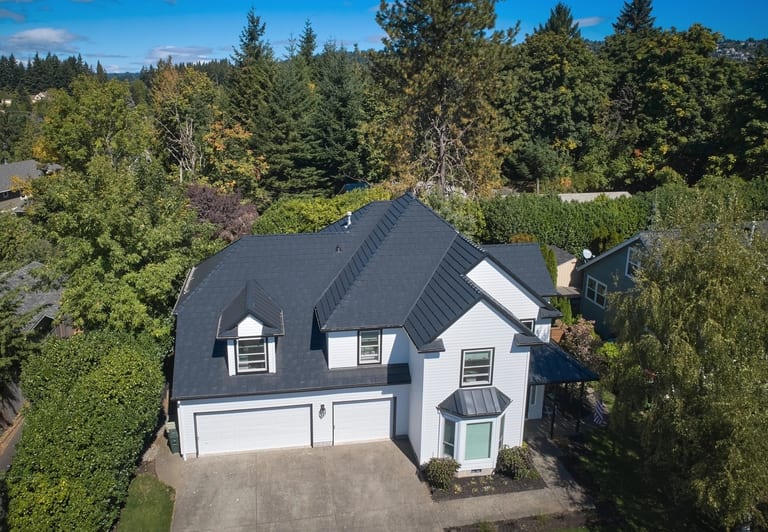 Deep Charcoal Interlock Shake aluminum roof on a white two-storey home with dormers among tall evergreens, Portland, Oregon