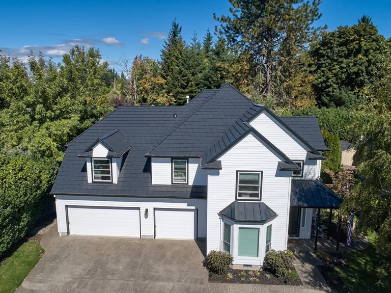 Deep Charcoal Interlock Shake aluminum roof on a white two-storey home with dormers among tall evergreen, Portland, Oregon