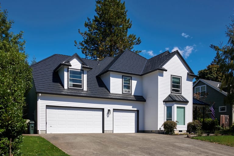 Deep Charcoal Interlock Shake aluminum roof on a white two-storey home with dormers among tall evergreens, Portland, Oregon