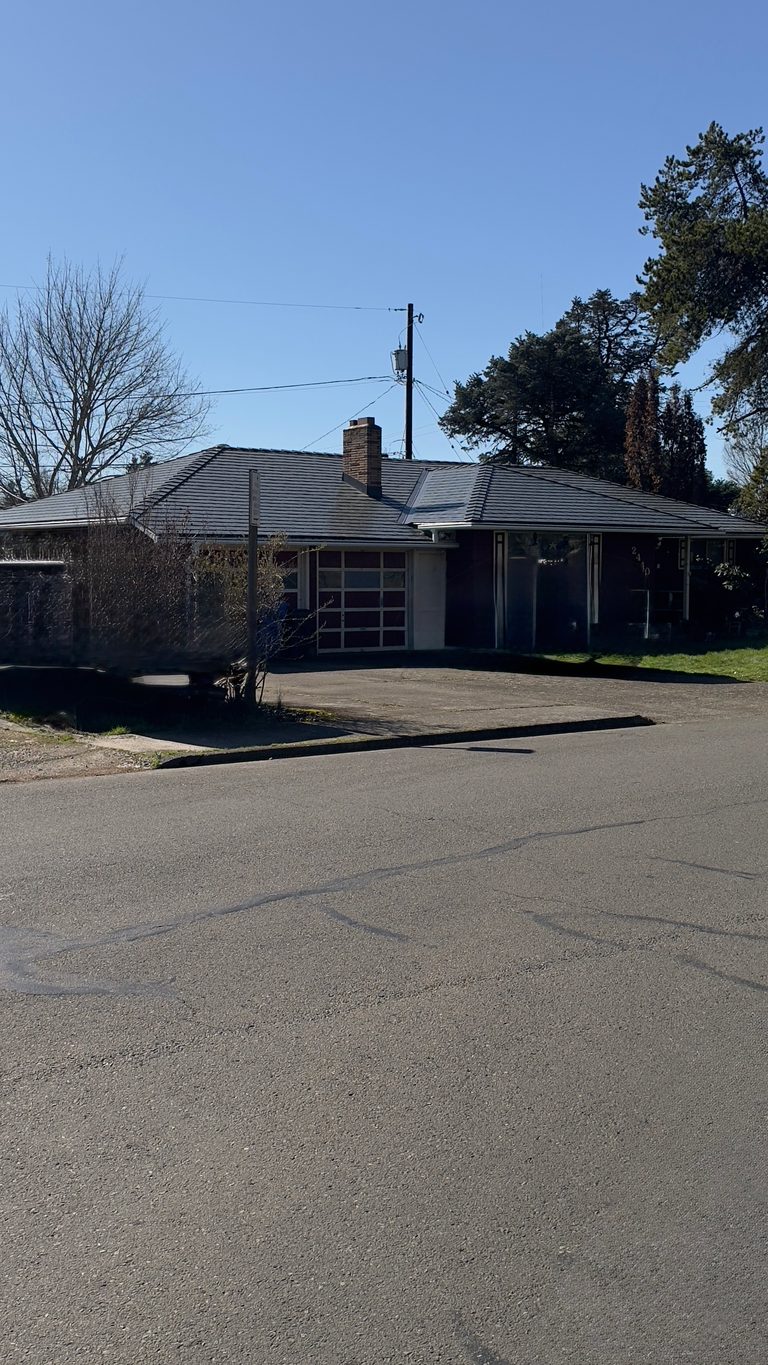 Single-story ranch home in Salem, OR with a multi-hip deep charcoal Interlock aluminum slate metal roof and brick chimney, viewed from across the street.