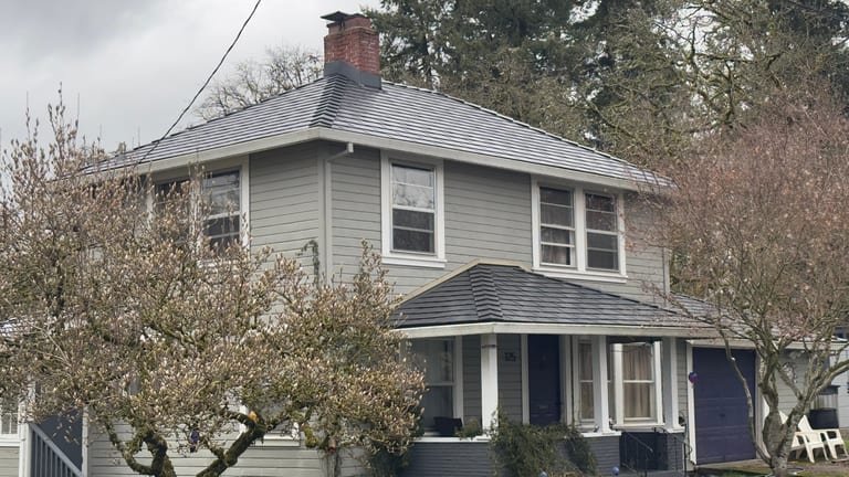 Two-story colonial home in St. Helens, OR with black Interlock aluminum slate metal roofing, multi-hip profile, brick chimney, and covered front porch.