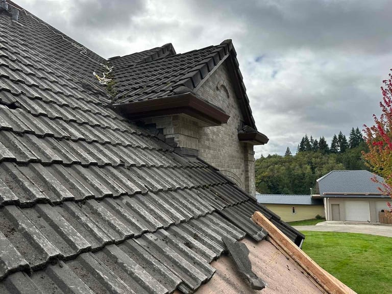 Close-up of black Interlock aluminum slate roof tiles on a steep multi-plane roof with stone dormer detail in Scappoose, OR.