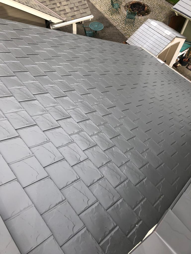 Close aerial view of Interlock aluminum slate roofing in Musket Grey on a residential hip roof in Scappoose, OR, showing wet tile texture detail.