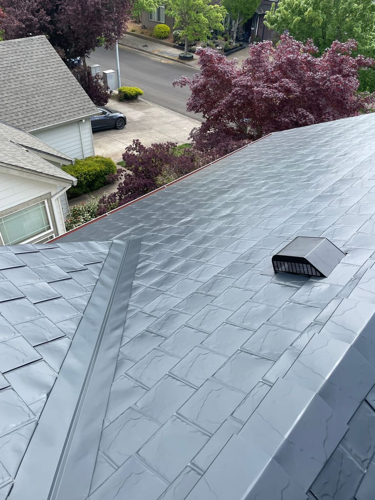 Aerial view of a dark charcoal Interlock aluminum slate metal roof with valley flashing and roof louver vent on a two-story suburban home in Hillsboro, OR.