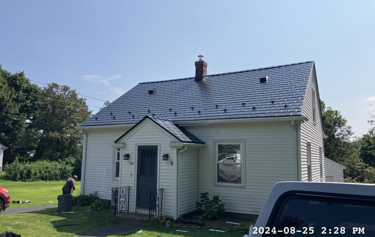 Cape Cod home with newly installed Interlock black aluminum slate metal roof, featuring a steep gable pitch, brick chimney, and small entry portico in Portsmouth, RI.