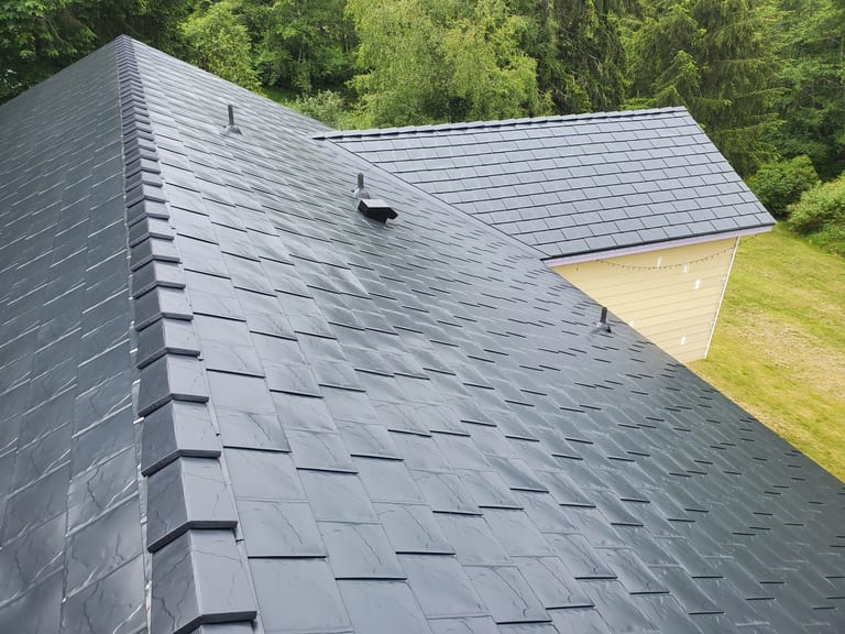 Black Interlock Slate aluminum roof on a dark two-storey home with dormers among tall conifers, Bremerton, Washington