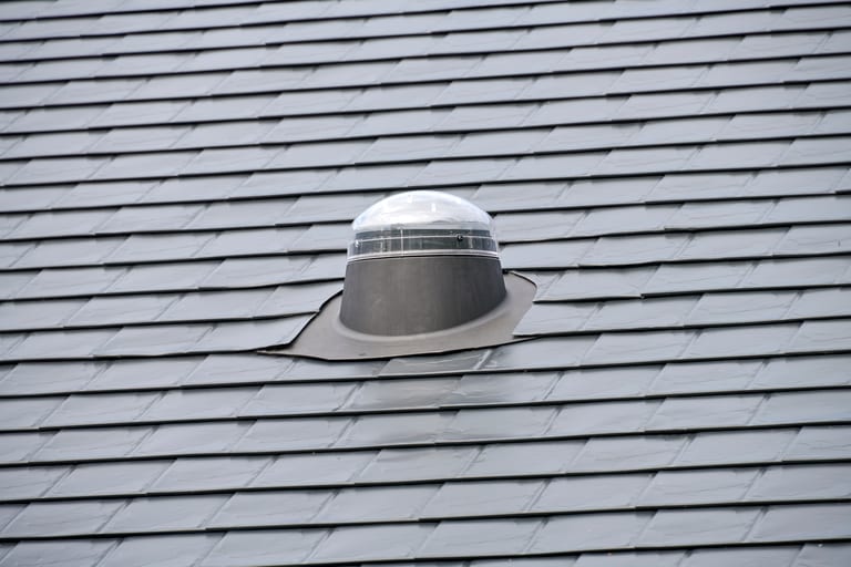 Close-up of a solar tube dome skylight with lead flashing installed on a dark grey Interlock aluminum slate metal roof.