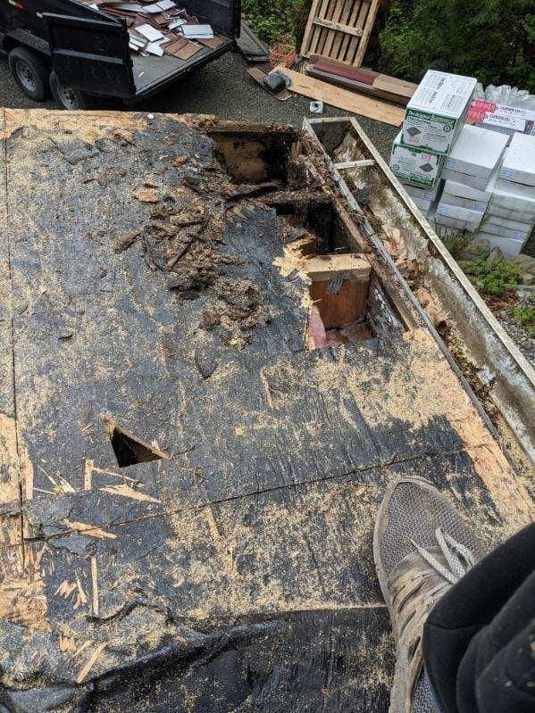 Severely deteriorated low-slope roof deck with rotted sheathing, holes, and debris exposed during tear-off before Interlock metal roofing installation.