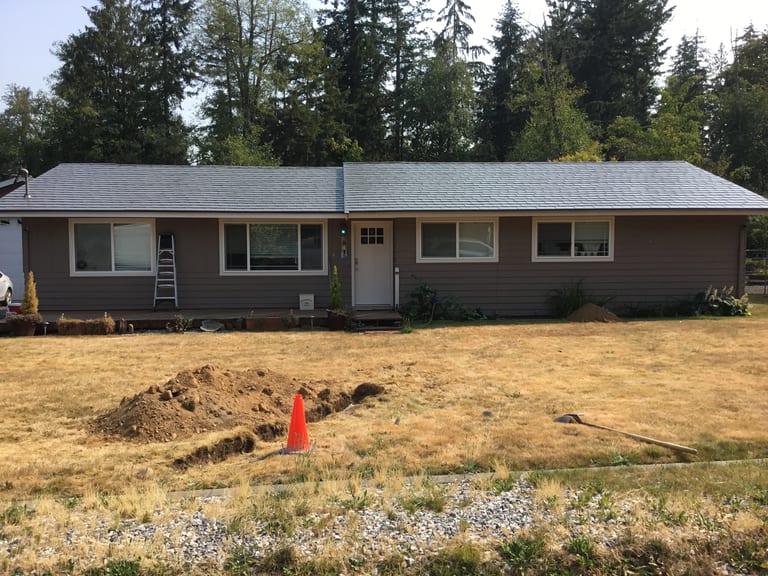After: Musket Grey Interlock Slate aluminum roof on a grey ranch-style home with a metal roof among evergreen, Bonney Lake, Washington