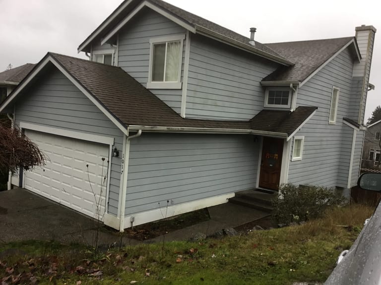 Deep Charcoal Interlock Slate aluminum roof on a grey two-storey home with dormers among tall pines, Silverdale, Washington