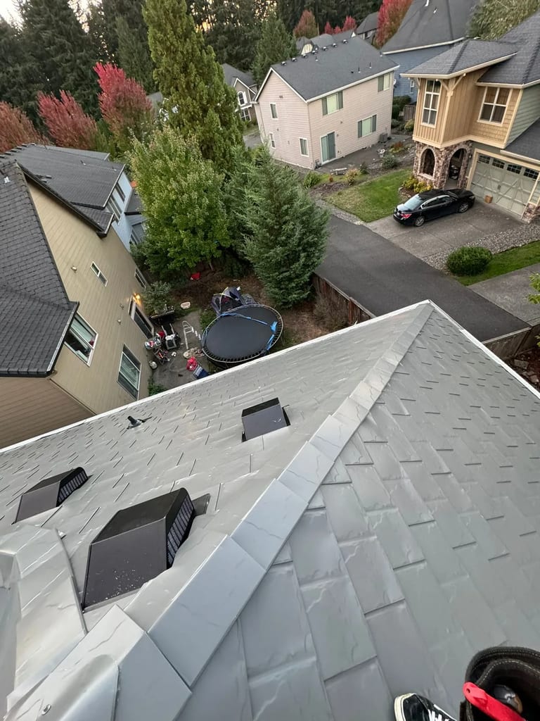 Aerial view of a Craftsman home with Interlock Musket Grey aluminum slate roofing, showing complex hip geometry, ridge caps, and roof vents in a suburban Vancouver, WA neighborhood.