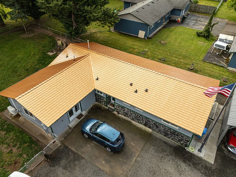 Aerial view of a single-story ranch home in Castle Rock, WA featuring a new Interlock aluminum slate roof in Copper Penny, with stone facade and American flag.