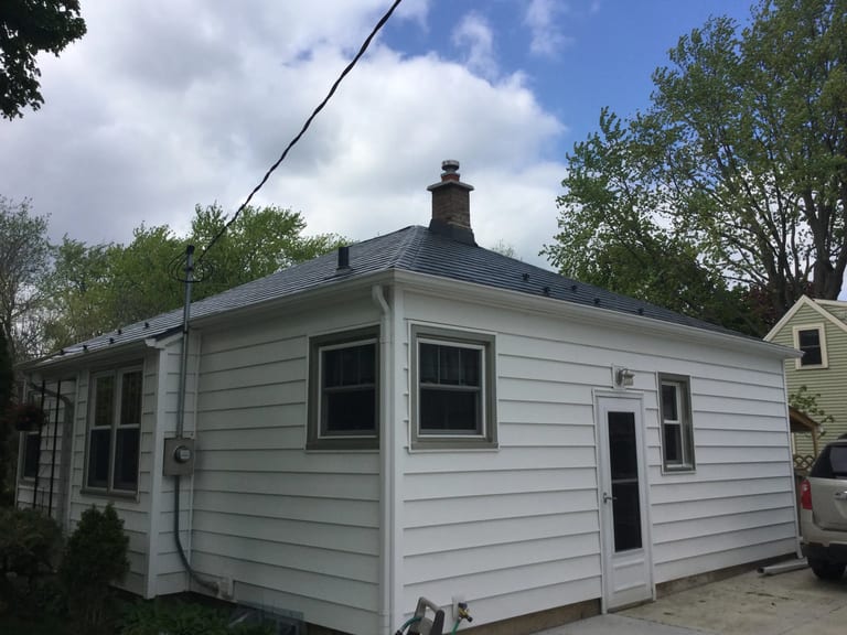 Charcoal Grey Interlock Slate aluminum roof on a white single-storey home with a metal roof among tall, Madison, Wisconsin