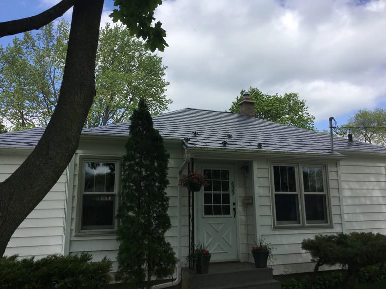 Charcoal Grey Interlock Slate aluminum roof on a white house with a metal roof among tall trees and bushes, Madison, Wisconsin