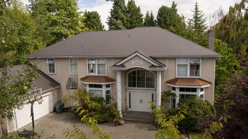 Tudor Brown Interlock Slate aluminum roof on a two-storey Tudor home with dormers among tall trees, Surrey, British Columbia