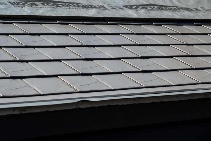 Taupe Interlock Slate aluminum roof on a taupe metal roof on a two-storey home among tall pines, Surrey, British Columbia