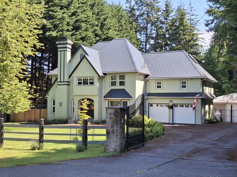 Deep Charcoal Interlock Slate aluminum roof on a beige two-storey home with dormers among tall pines, Bowser, British Columbia