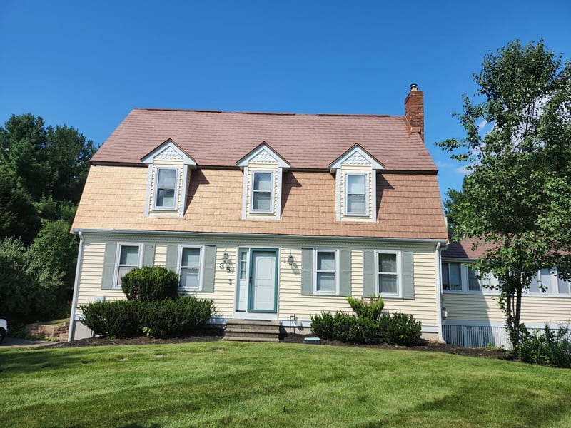 Aged Copper Interlock Shingle aluminum roof on a yellow two-storey Colonial home with dormers among tall, Wrentham, Massachusetts
