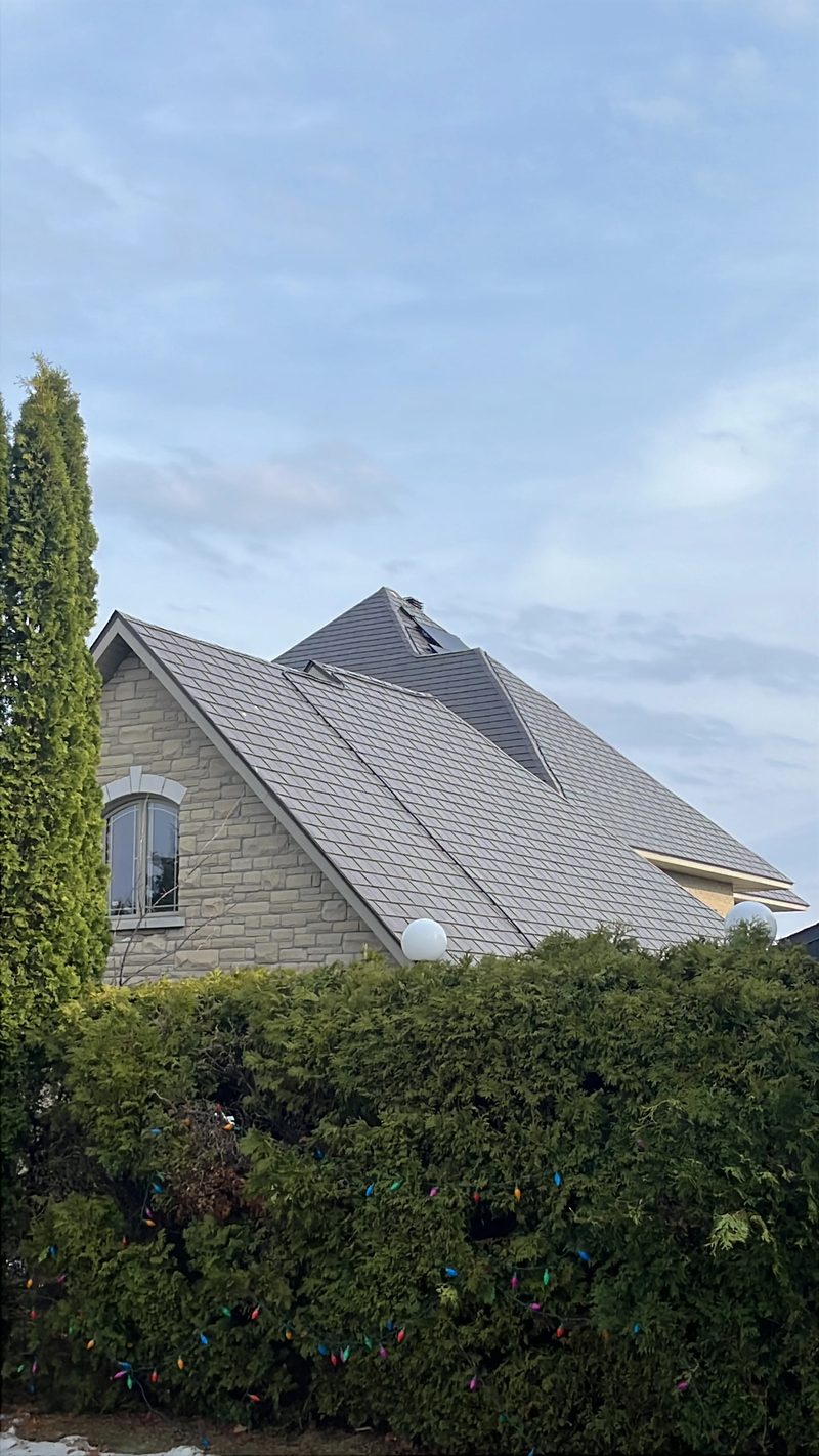 Tudor Brown Interlock Slate aluminum roof on a brown two-storey Tudor home with dormers among tall pines, Sudbury, Ontario