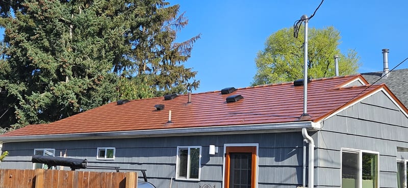 Copper Penny Interlock Slate aluminum roof on a grey one-storey home with a metal roof among trees, Portland, Oregon